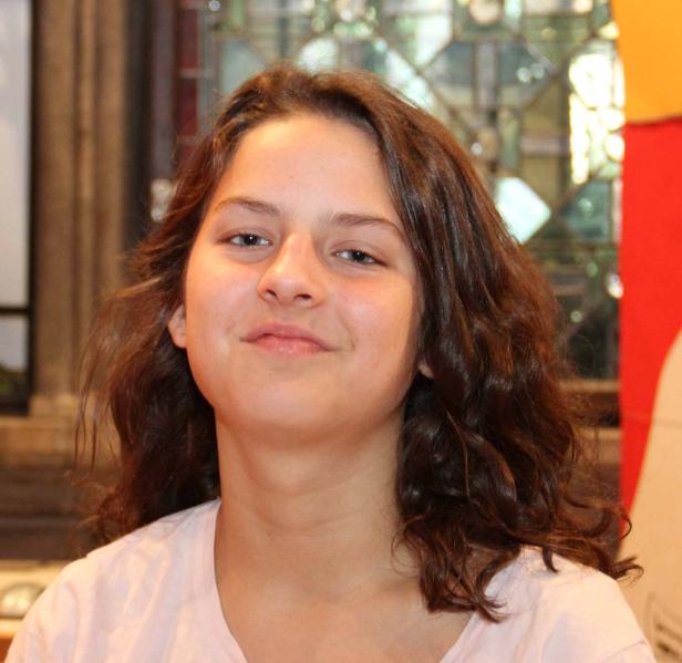 Ein Porträt einer jungen Frau mit braunen, gewellten Haaren.