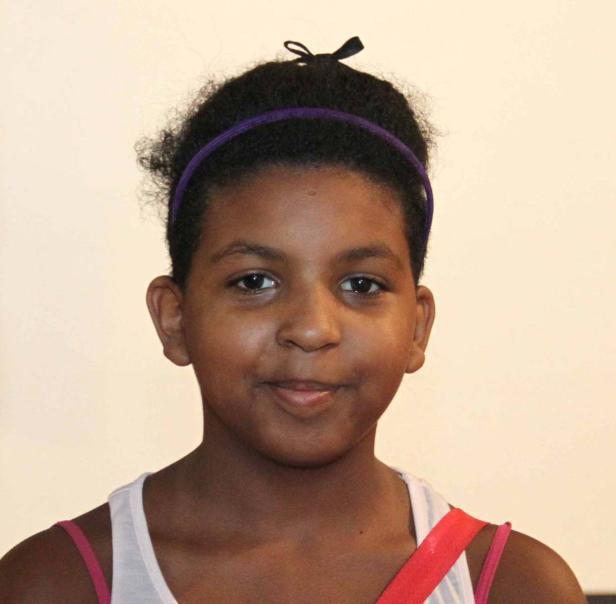 Ein junges Mädchen mit einem lila Stirnband lächelt in die Kamera.