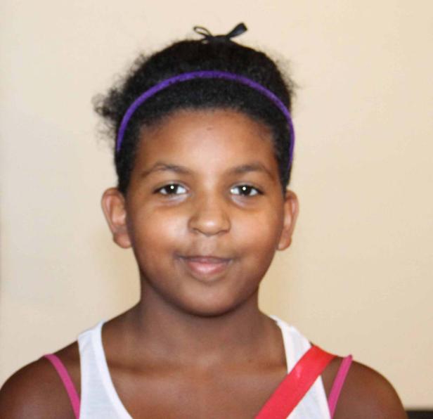 Ein junges Mädchen mit einem lila Stirnband lächelt in die Kamera.