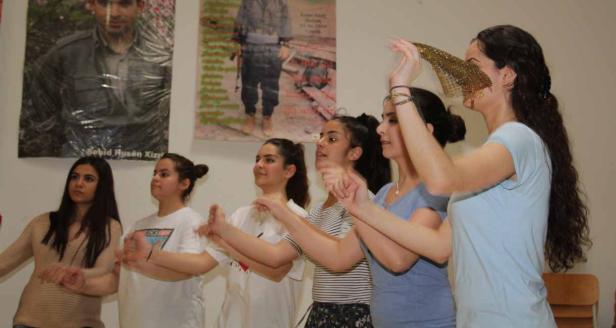 Eine Gruppe junger Frauen tanzt vor Postern an einer Wand.