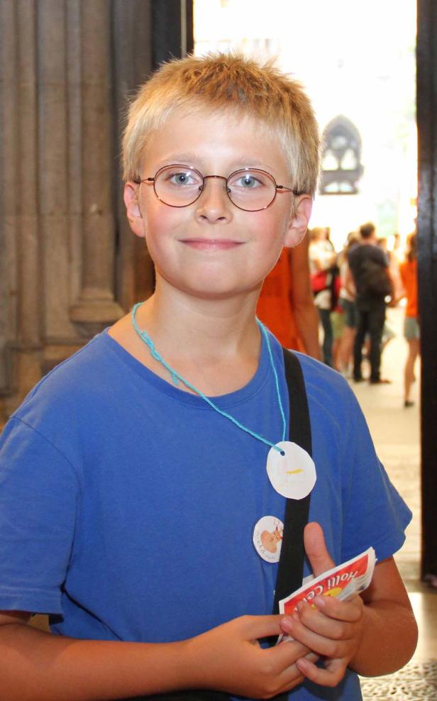 Ein lächelnder Junge mit Brille und blauem T-Shirt steht in einem Gebäude.