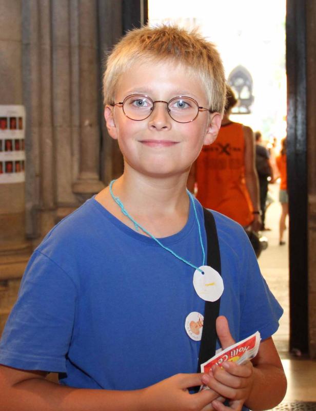 Ein lächelnder Junge mit Brille und blauem T-Shirt steht in einem Gebäude.