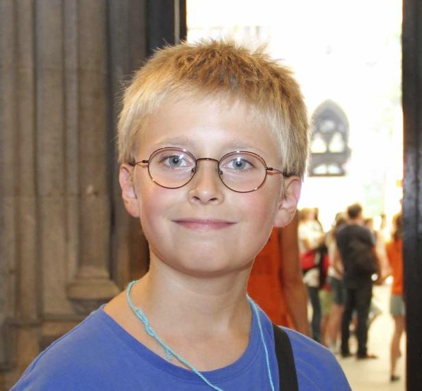 Ein lächelnder Junge mit blonden Haaren und runder Brille.