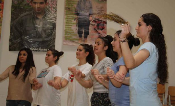 Eine Gruppe junger Frauen tanzt vor Porträts an einer Wand.