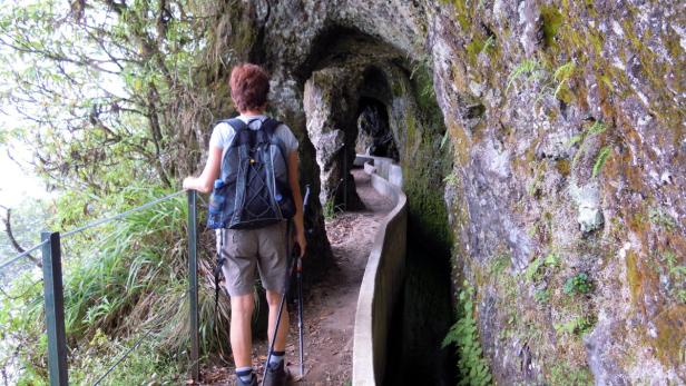 Eine Wanderin auf einem Pfad entlang einer Levada auf Madeira.