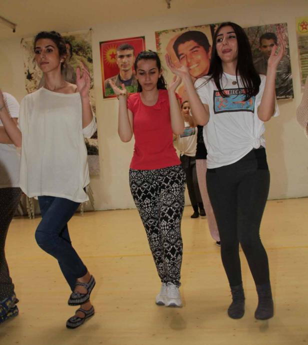 Eine Gruppe junger Frauen tanzt vor Postern an einer Wand.