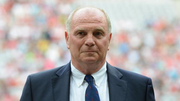 Uli Hoeneß in einem dunklen Anzug mit Krawatte vor unscharfem Hintergrund.