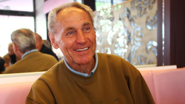 Ein lächelnder älterer Mann sitzt in einem Restaurant.