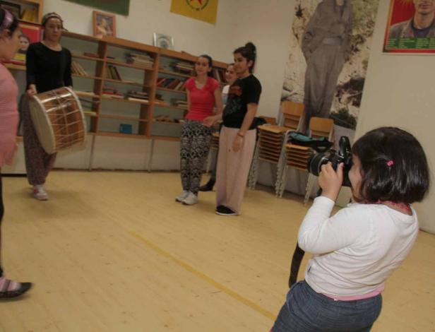 Eine Gruppe junger Frauen in einem Raum, eine davon mit einer Trommel, während ein Mädchen sie fotografiert.