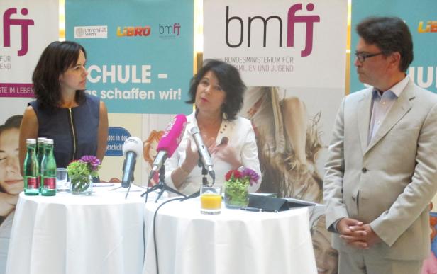 Drei Personen stehen hinter Tischen mit Mikrofonen bei einer Veranstaltung des Bundesministeriums für Familien und Jugend.