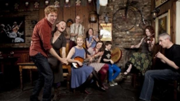 Eine Gruppe von Menschen spielt traditionelle irische Musik in einem Pub, während ein Paar tanzt.