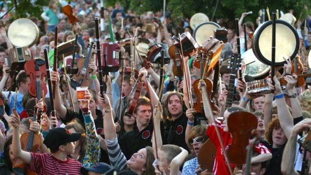 Eine Menschenmenge hält Musikinstrumente wie Geigen und Trommeln in die Luft.
