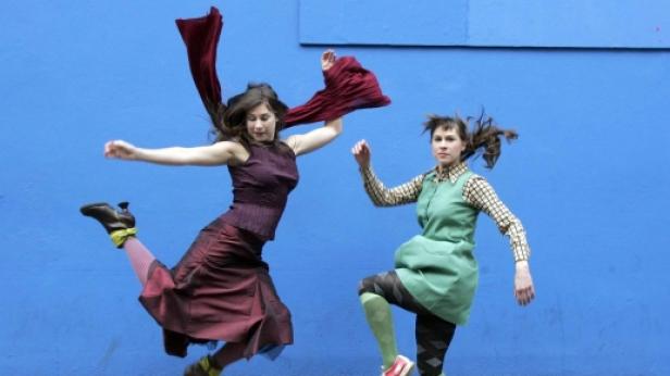 Zwei Frauen springen vor einer blauen Wand in die Luft.