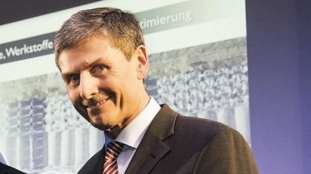 Ein Mann mit Anzug und Krawatte lächelt vor einer Präsentationswand.