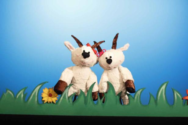 Lisa und der Krachdrache Zwei Ziegenpuppen stehen vor einem blauen Hintergrund mit Gras und Blumen.