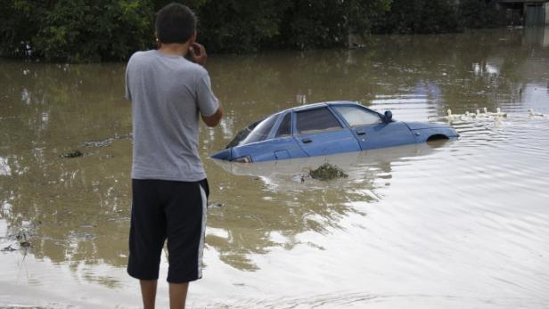 Ein Mann steht im Hochwasser und fotografiert ein blaues Auto, das fast vollständig überflutet ist.