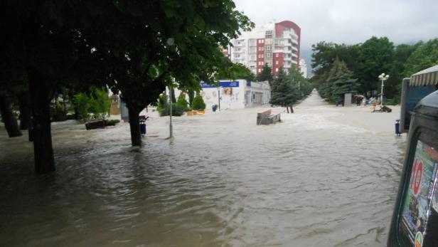 Ein überfluteter Park mit Wasser, das über die Wege und Grünflächen fließt.