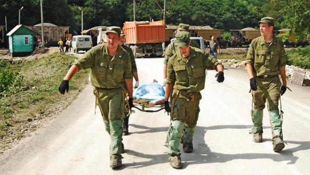 Soldaten tragen eine Person auf einer Trage über eine Straße.