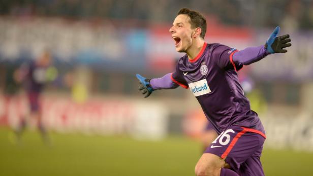 Ein Fußballspieler in lila Trikot jubelt mit ausgestreckten Armen.