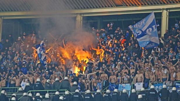 Fußballfans zünden Bengalos im Stadion, während Polizisten im Vordergrund stehen.
