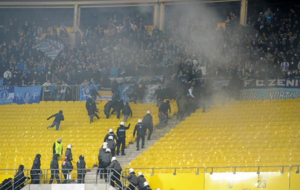 Polizisten schreiten in einem Stadion mit gelben Sitzen gegen Fans ein.