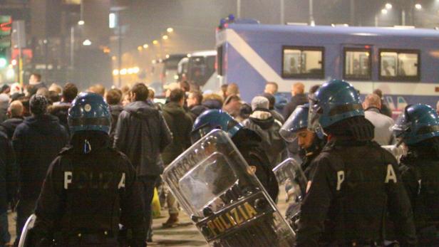 Polizisten stehen mit Schilden vor einer Menschenmenge.