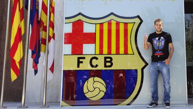 Ein Mann posiert vor dem FC Barcelona-Logo mit erhobenem Daumen.