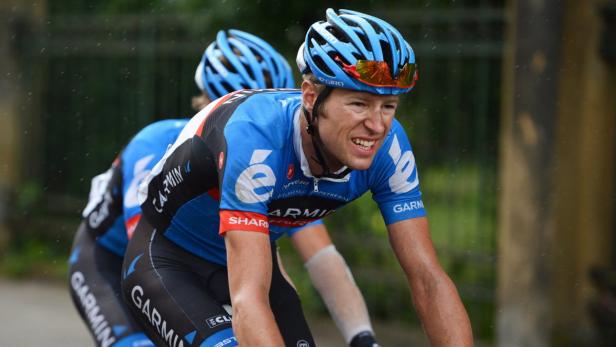 Ein Radfahrer in blauem Trikot und Helm fährt im Regen.