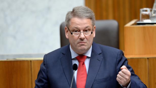 Ein Mann mit Brille und Anzug gestikuliert vor einem Mikrofon.