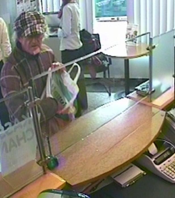 Ein älterer Mann mit karierter Mütze steht an einem Schalter mit einer Plastiktüte in der Hand.