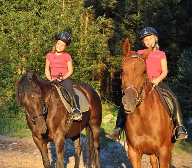 Zwei Mädchen reiten auf ihren Pferden durch den Wald.