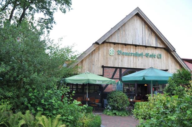 Der Bauernhof-Café G mit Außenterrasse und grünen Sonnenschirmen.