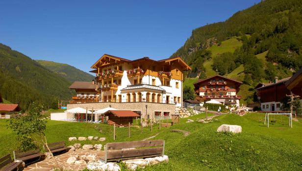 Ein Hotel im Chalet-Stil liegt in einer grünen Berglandschaft.