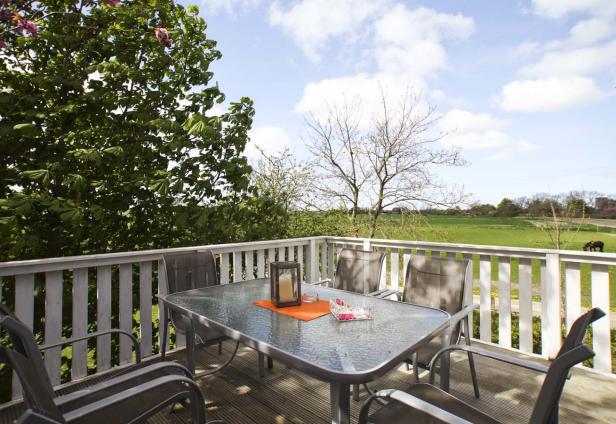 Ein Tisch und Stühle stehen auf einer Terrasse mit Blick auf eine grüne Landschaft.