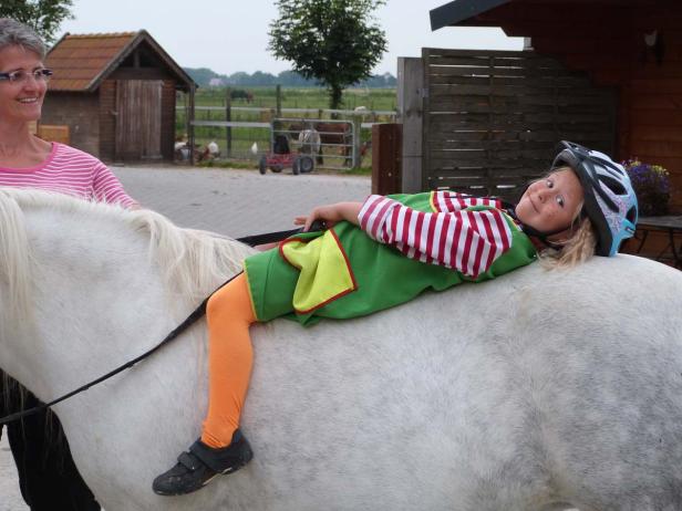 Ein Mädchen im Kostüm liegt auf dem Rücken eines weißen Pferdes.
