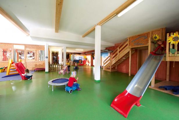 Mehrere Kinder spielen in einem hellen, farbenfrohen Spielzimmer mit Rutschen und Spielzeugen.
