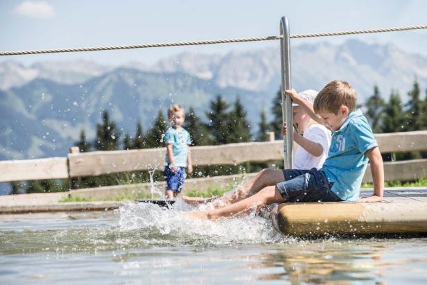 Zwei Jungen sitzen an einem sonnigen Tag auf einer Art Floß und planschen im Wasser.