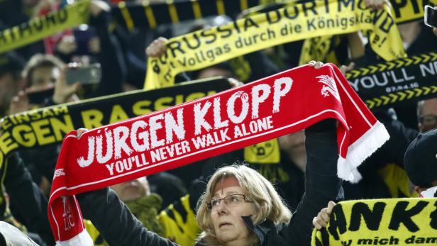 Eine Frau hält einen roten Schal mit der Aufschrift „Jürgen Klopp – You'll Never Walk Alone“ in die Höhe.