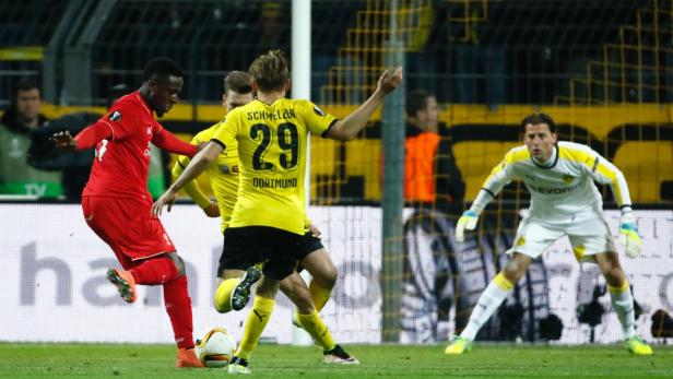 Ein Fußballspieler in Rot schießt den Ball, während ein Torwart in Gelb zusieht.