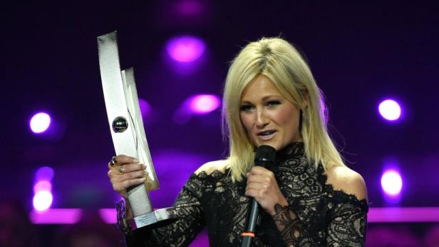 Helene Fischer hält eine Trophäe und ein Mikrofon in der Hand.