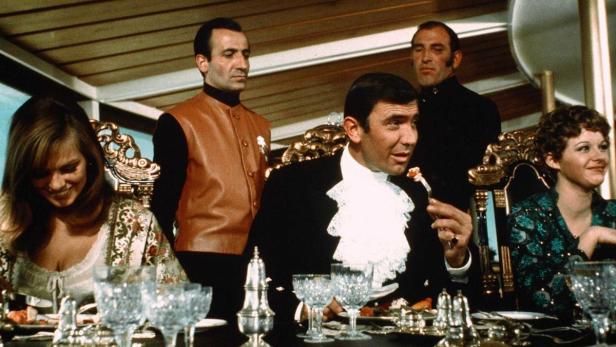 Roger Moore als James Bond bei einem Abendessen mit Gästen.
