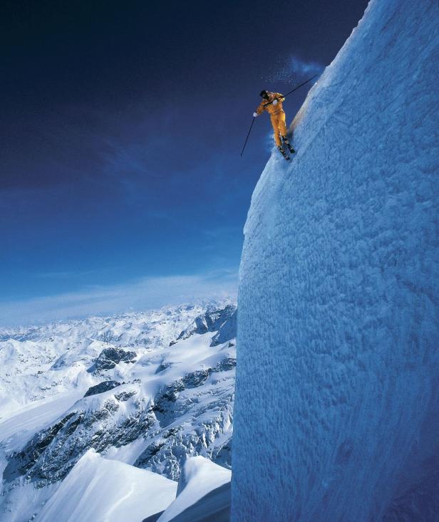 Ein Skifahrer in gelber Kleidung fährt einen steilen, schneebedeckten Hang hinunter.