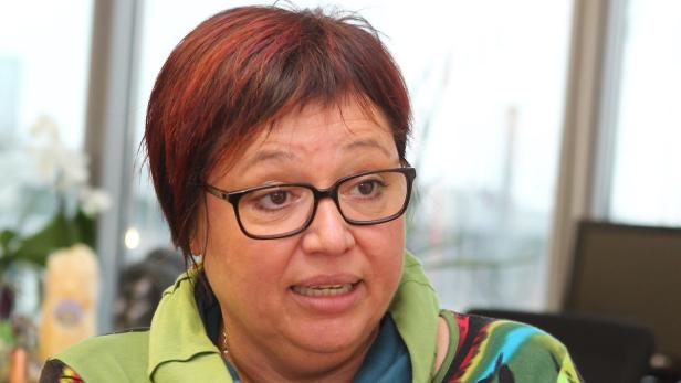 Eine Frau mit rotbraunen Haaren und Brille schaut aufmerksam zur Seite.