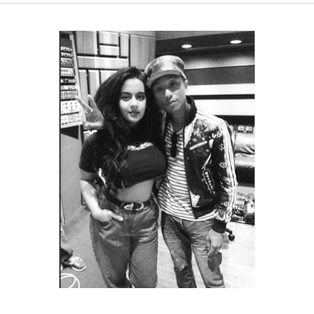 Eine Frau mit Victory-Zeichen posiert mit Pharrell Williams in einem Musikstudio.