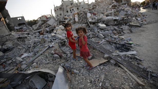 Zwei kleine Mädchen stehen vor den Trümmern zerstörter Gebäude.