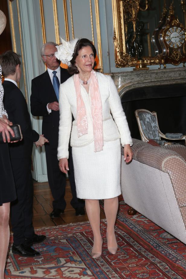 Königin Silvia von Schweden in einem weißen Kostüm mit rosa Schal.