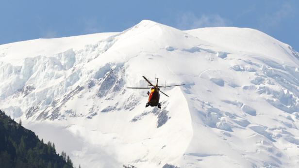 Mit Hubschrauber wird nach den Bergsteigern gesucht, im Hintergrund der Mont Maudit Ein rot-gelber Hubschrauber fliegt vor einem schneebedeckten Berg.