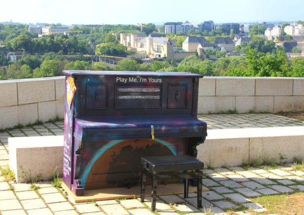 Ein bunt bemaltes Klavier mit der Aufschrift „Play Me, I'm Yours“ steht im Freien.