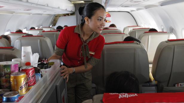 Eine Stewardess schiebt einen Servierwagen mit Getränken in einem Flugzeug entlang.