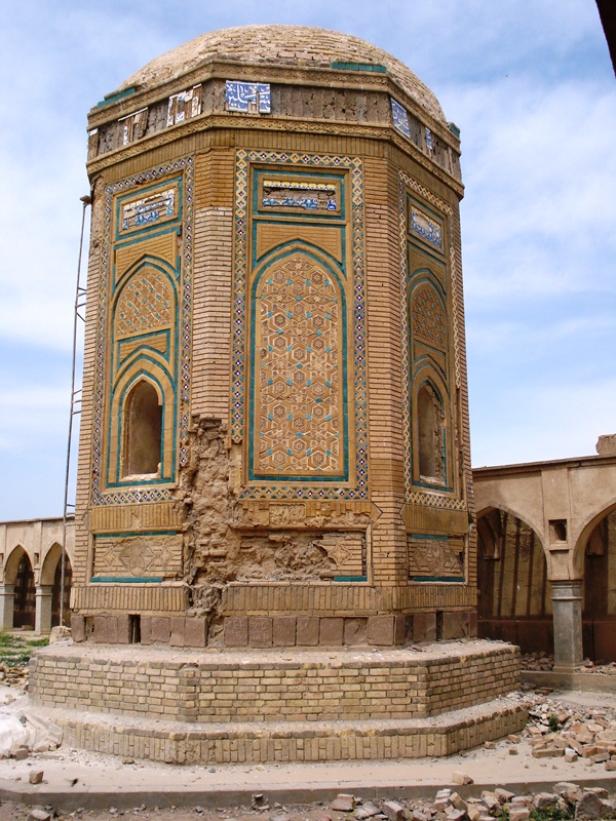 Ein achteckiges, ziegelgemauertes Mausoleum mit islamischen Mustern und teilweisen Zerstörungen.